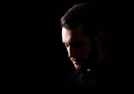 sad young man with a beard on a black background