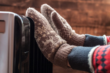 Women's hands in Christmas, warm, winter mittens on the heater. Keep warm in the winter, cold evenings. Heating season