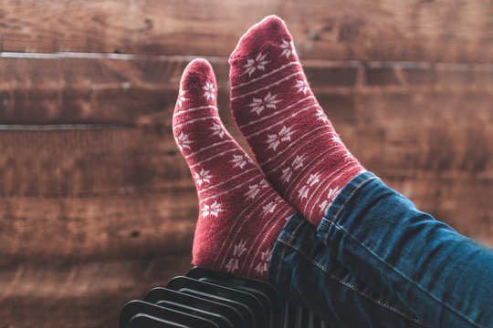 Women's feet in Christmas, warm, winter socks on the heater. Keep warm in the winter, cold evenings. Heating season
