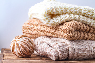 Warm, pastel clothes, knitted, pastel-colored scarves and a ball of knitting yarn on a white background. Winter, autumn clothes.
