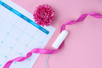 Regular menstrual cycle. Tampons, women's calendar, flowers on a pink background. Hygiene care during critical days. Women's and gynecological health care. Hygiene