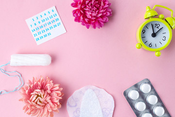 Tampons for menstruation, alarm clock, women's calendar, feminine pads, pain pills for critical days and flowers on a pink background. Regular menstrual cycle. Copy space