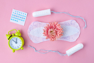 Tampons for menstruation, alarm clock, women's calendar, feminine pads and a pink flower on a pink background. Hygiene care during critical days. Regular menstrual cycle.