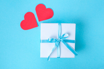 Gift, small box tied with a satin blue ribbon and red hearts on a blue background. Gift concept. Surprises and gifts for loved ones. Congratulations on the holiday