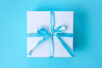 Gift, small box tied with a satin blue ribbon on a blue background. Gift concept. Surprises and gifts for loved ones