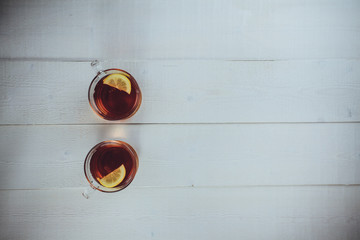 Two full cups of black tea with lemon, on white wooden background top view, isolated
