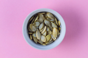 Peeled pumpkin seeds in a white saucer on a pink background