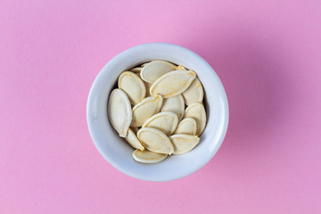 Pumpkin seeds in small saucer on a pink background