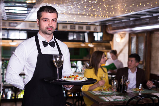 Portrait of frendly male waiter who is standing with tray