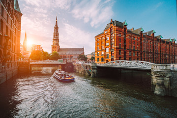 Touristic cruise boat on a channel with bridges in the old warehouse district Speicherstadt in Hamburg in golden hour sunset light, Germany - obrazy, fototapety, plakaty