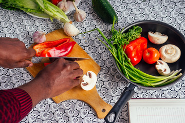 closeup of man hands african american cuts vegetables fry salad pepper, mushrooms, tomato in...