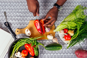 closeup of man hands african american cuts vegetables fry salad pepper, mushrooms, tomato in...