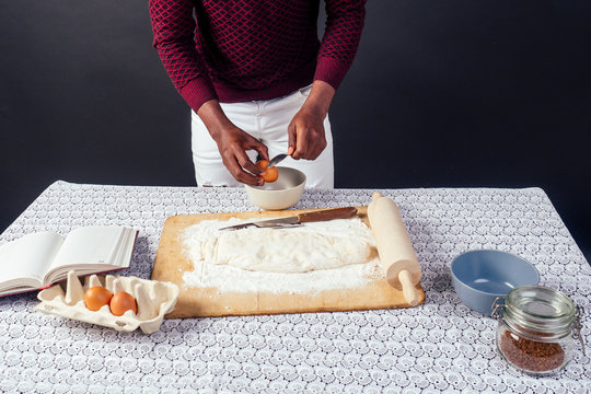 African American male cook chef boasts of pastry hands in flour baking .man`s hands sheets dough with rolling pin bakes cake , the eggs and recipe book on the table. homemade baking
