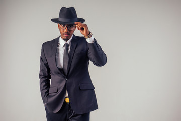 Retro style African american business man model in dark suit and black hat in studio on white background