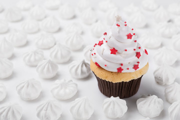 homemade cupcake with white cream, decorated with red stars surrounded by white meringues, on a white background, concept of birthday or christmas