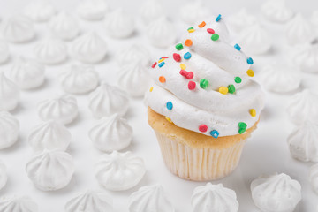 minimal concept of a bright holiday, beautiful homemade cupcake with white cream surrounded by white meringues, on a white background, birthday or Christmas