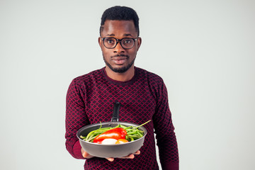 african american chef kitchener holding a frying pan wizard man cooking magic flying food salad, carrot, garlic, onion, pepper, potato, cucumber isolate white background studio.magic of taste fantasy