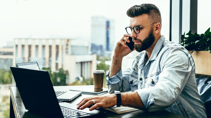 Bearded businessman,blogger sitting in cafe,talking on smart phone,working on laptop, freelancer working in coffee shop.