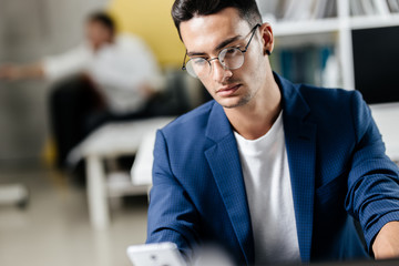 Professional young architect in glasses dressed in blue checkered jacket  works on the laptop in the office