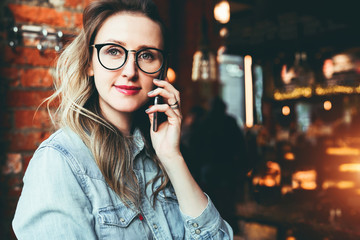 Young businesswoman has telephone conversations.Cheerful girl blogger in trendy glasses sitting in cafe,talking on phone