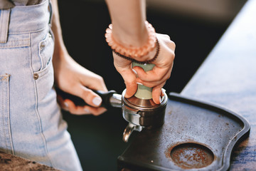 A young pretty slim girl,wearing casual outfit,is cooking coffee in a modern coffee shop. It focuses on the process.