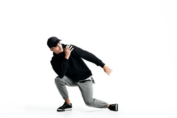 Handsome young man wearing a black sweatshirt, gray pants and a cap dancing street dances on a white background