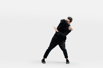 Dark-haired stylish man dressed in a stylish black clothes is dancing street dance. He makes stylized movements with his hands