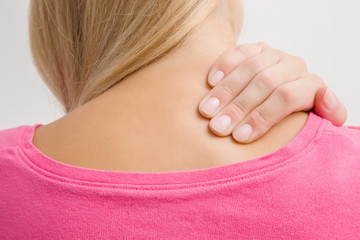 Young, blonde woman massaging her shoulder with hand. Pain from strain of sedentary long work, overwork, and incorrect posture. Inactive lifestyle.