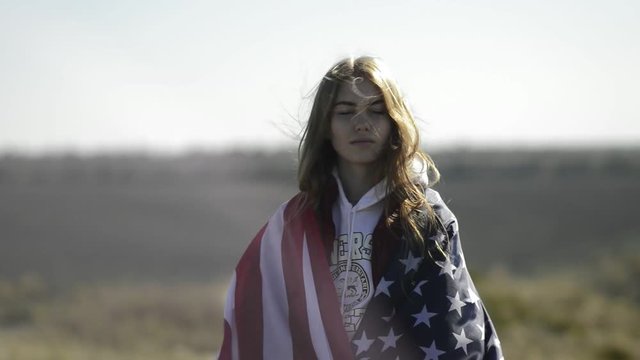A young beautiful girl is holding a USA flag, which is developing in the wind.