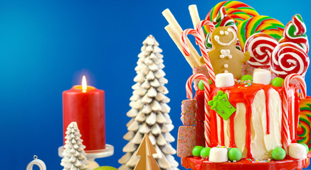 On trend festive candyland Christmas drip cake on blue background.