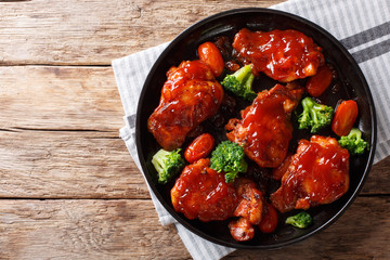 Sweet-sour glazed chicken with spicy sauce, broccoli and tomatoes close-up on a plate. horizontal top view