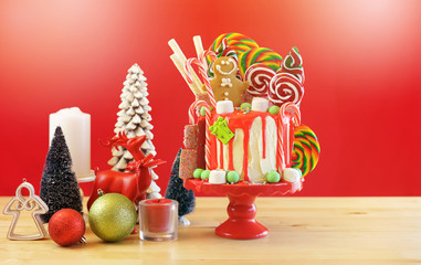 On trend festive candyland Christmas drip cake on red background.