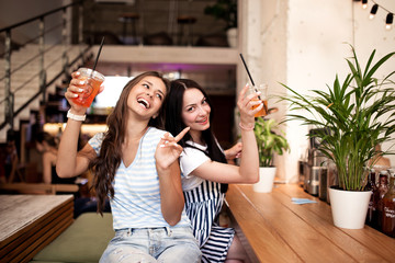 Two pretty youthful smiling girls,dressed in casual outfit,sit next to each other and look at the...