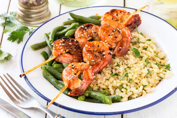 Buddha bowl with brown rice, green beans and shrimp skewers on white wooden table