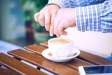Young man hands holding sugar bag and sweetens coffee in a cafe.