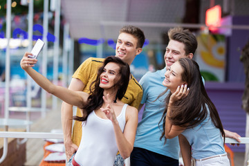 A company of good-looking friends is laughing and making selfie in the nice summer cafe. Entertainment, having good time. Friendship.