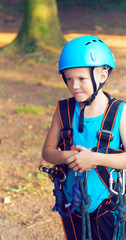 Cute little boy in blue shirt and helmet having fun at the adventure park, holding ropes and prepering to climb wooden stairs. Hobby, active lifestyle concept.