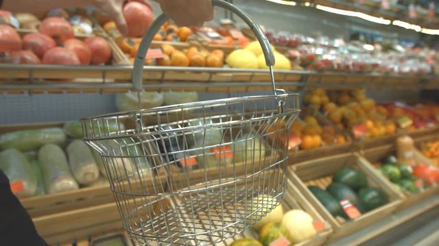 Fruit basket in the supermarket.
Men's hands carry a grocery basket in the supermarket and put different fruits in it: pomegranate, melon, oranges, tangerines.