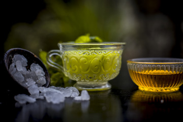 Iced cucumber and mint tea on wooden surface in a transparent cup with slices of cucumber and raw cucumber,mint leaves,sugar and honey with green tea in a separate glass cup.