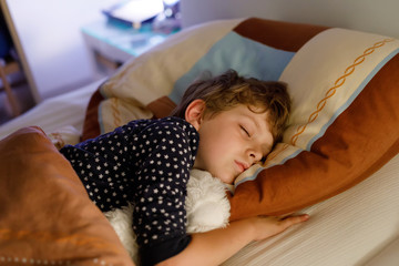 Little preschool kid boy sleeping in bed with colorful lamp.