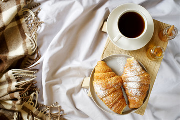 Croissants and coffee for breakfast in bed. Concept of cozy holiday
