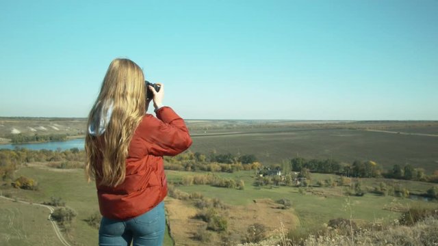 Young beautiful girl makes photos of the surrounding landscape. Girl you are a hill. Sunny day. Rest and travel.