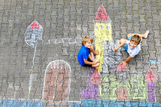 Two little kids boys drawing knight castle with colorful chalks on asphalt. Happy siblings and friends having fun with creating chalk picture and painting. Creative leisure for children in summer.