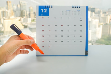 close up woman holds orange highlighter pen in hand to mark on appointment and meeting date on December calendar