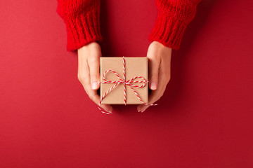 Female's hands in red pullover holding Christmas gift box on red background. Christmas and New Year...