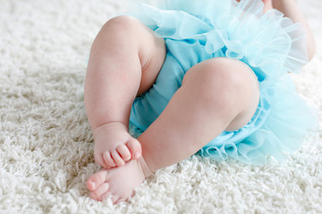 Obraz na płótnie Canvas Closeup of legs and feet of baby girl on white background wearing turquoise tutu skirt.