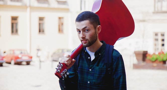 Young musician walking with a guitar on his shoulder. Music, art, creativity concept.
