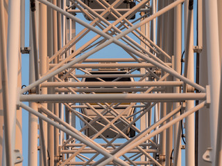 Low angle shot to a part of big wheel in playground park. Worm eye view Image of Ferris wheel. Uprise to look at a part of machine in sunny day. Take angle elevation to a beautiful blue sky.