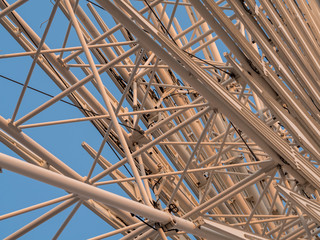 Low angle shot to a part of big wheel in playground park. Worm eye view Image of Ferris wheel. Uprise to look at a part of machine in sunny day. Take angle elevation to a beautiful blue sky.