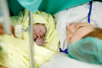Newborn baby wrapped in blankets after birth. Mother looking for the first time on new born daughter